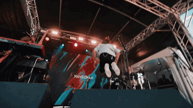 a man is jumping in the air on a stage with a mansionair sign in the background