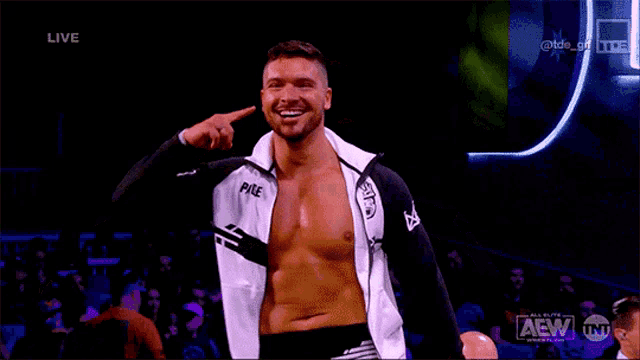 a shirtless wrestler is smiling and pointing at his head while wearing a jacket that says pike