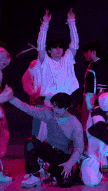 a group of young men are dancing on a stage with purple lights behind them