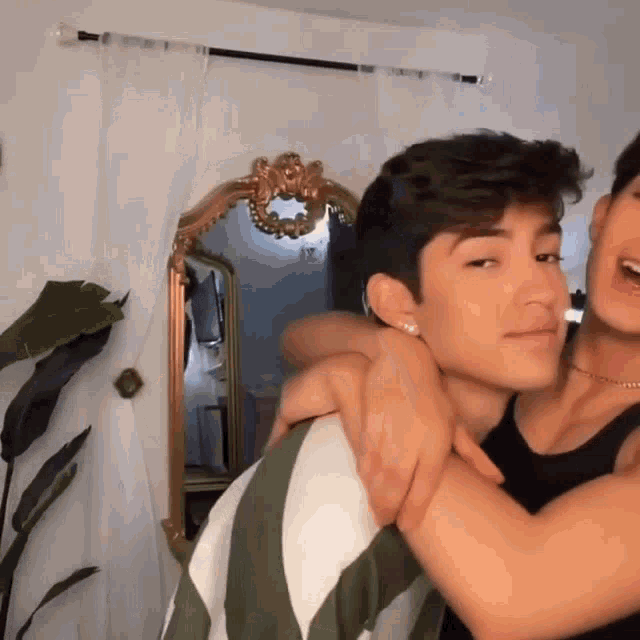 two young men are hugging each other in front of a mirror in a room .