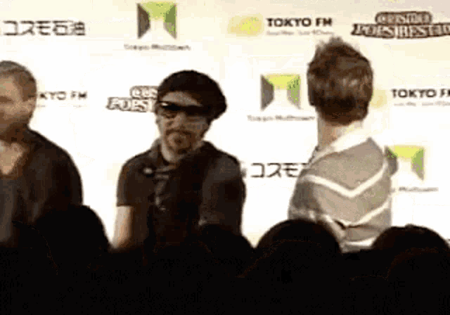 a group of people are standing in front of a wall that says tokyo fm .