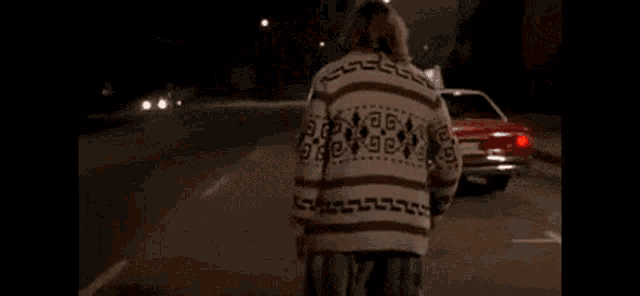 a man in a striped sweater is standing next to a red car on the side of the road .