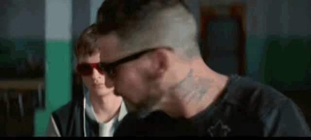 a man with a tattoo on his neck is talking to another man wearing sunglasses .