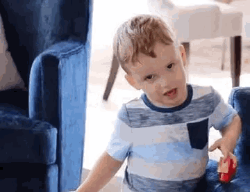 a young boy is sitting on a blue chair playing with a red toy .