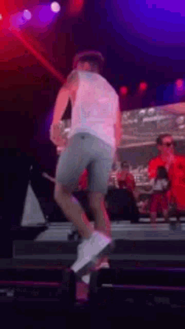 a man in shorts and a white tank top is dancing on a stage .