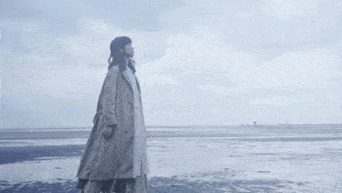 a woman in a trench coat is standing on a concrete wall overlooking a body of water