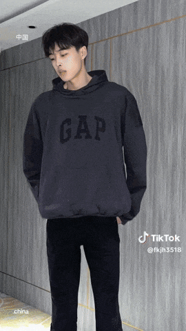 a man wearing a gap hoodie stands in front of a wooden wall