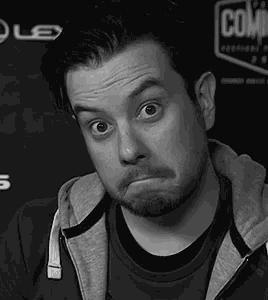 a man with a beard is wearing a hoodie and making a funny face .