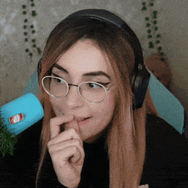 a woman wearing glasses and headphones has a sticker on her finger that says coca cola