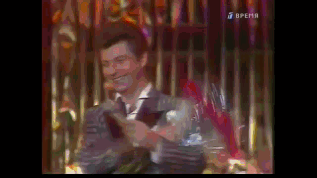 a man in a suit is holding a microphone in front of a curtain that says " время " on it