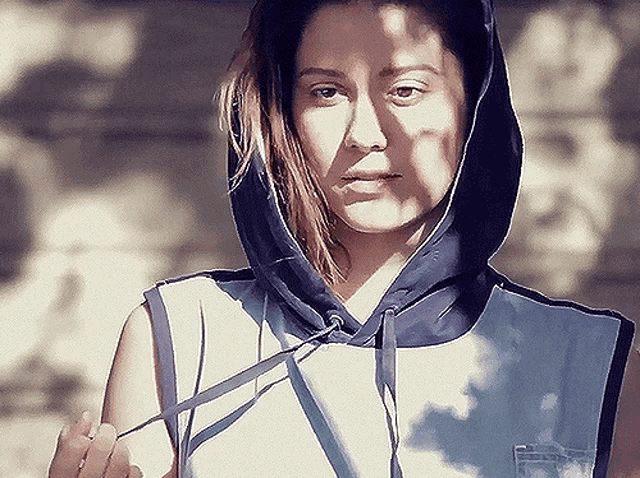 a woman wearing a hooded top is standing in the sunlight