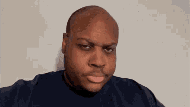 a bald man is making a funny face and pointing at the camera with his finger .