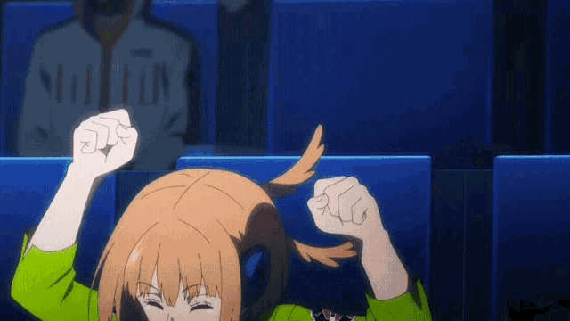 a girl in a green shirt is raising her fist in the air while sitting in a theater