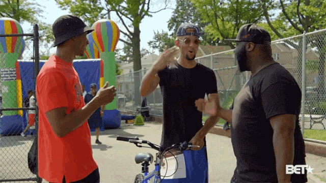 three men are standing in front of a fence with a bet logo on the bottom right