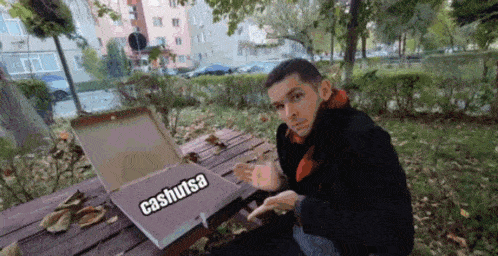 a man is sitting at a picnic table with a pizza box that says cashutsa on it