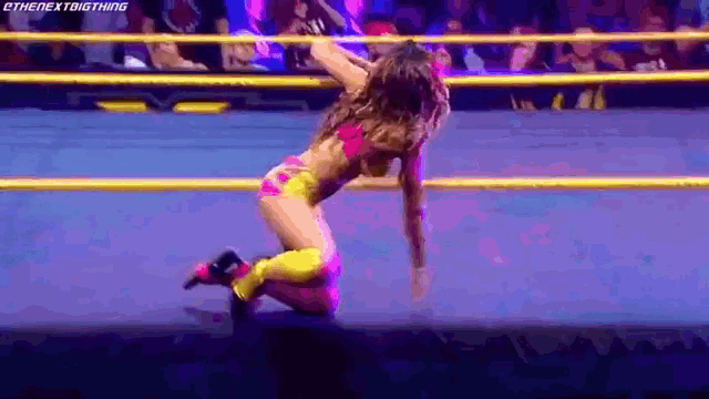 a woman is kneeling down in a wrestling ring while a crowd watches .