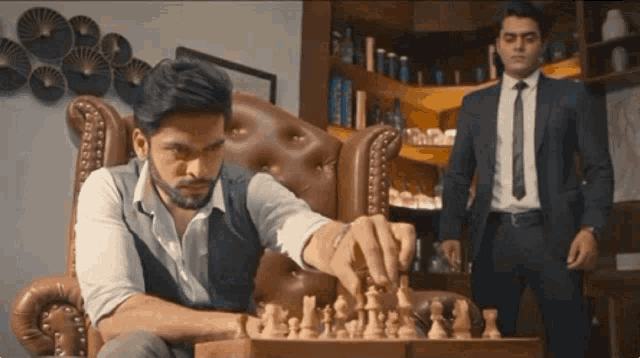 a man in a suit is playing a game of chess while another man watches