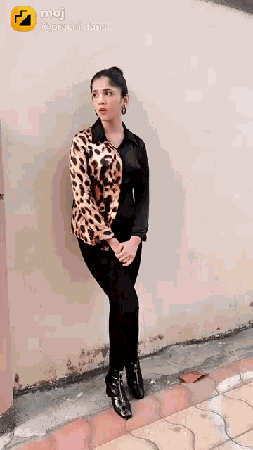 a woman in a leopard print shirt and black pants stands in front of a wall .
