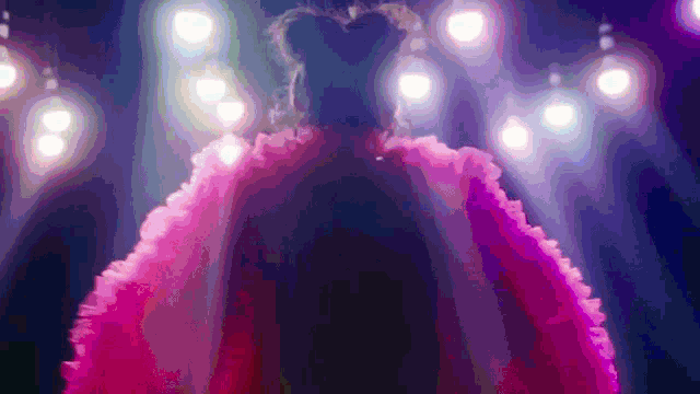 a woman in a pink dress is standing on a stage in front of lights