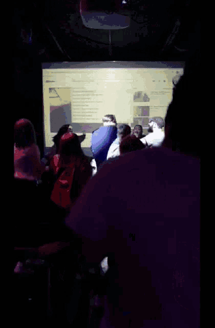 a crowd of people are dancing in front of a large screen