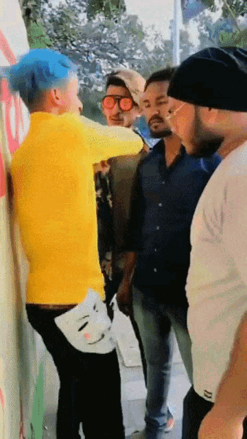 a group of men are standing around a man with blue hair and a yellow shirt