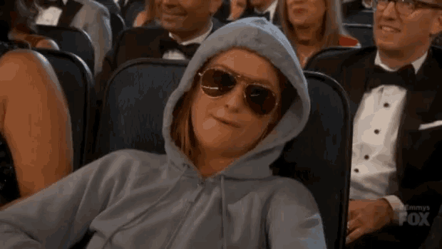 a woman wearing sunglasses and a hoodie is sitting in a crowd of people watching a movie .