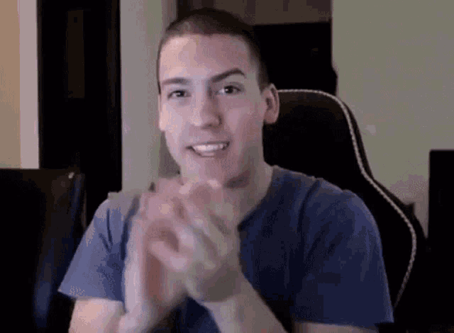 a man in a blue shirt is clapping his hands in front of a computer .