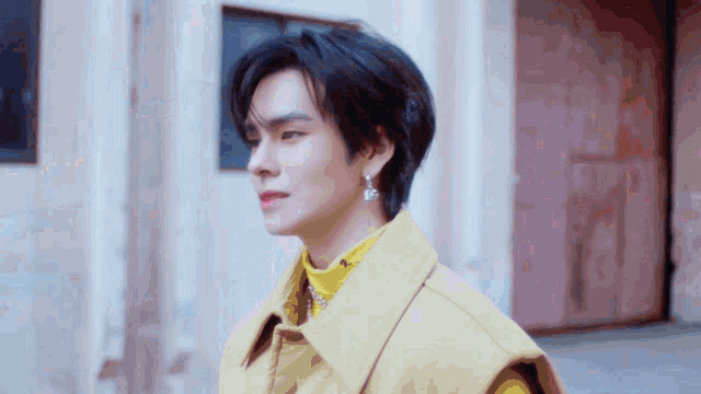 a man wearing a yellow vest and earrings looks to the side