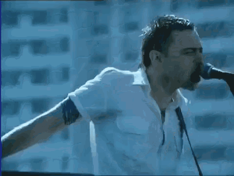 a man in a white shirt singing into a microphone with his arms outstretched