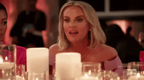 a woman is sitting at a table with candles and glasses in front of her .