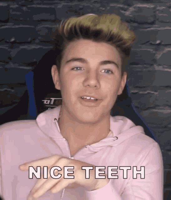 a young man wearing a pink hoodie is sitting in a chair and says nice teeth .
