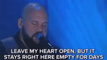 a bald man with a beard is singing into a microphone with a blue background .