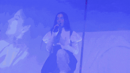 a woman singing into a microphone in front of a projection of another woman 's face