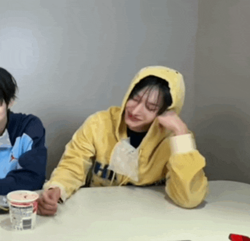 a woman wearing a yellow hoodie is sitting at a table with a cup of coffee .