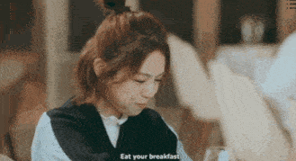 a woman is sitting at a table with the words eat your breakfast written on the screen