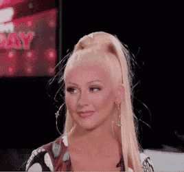 a woman with blonde hair in a ponytail and hoop earrings is smiling in front of a tv screen .