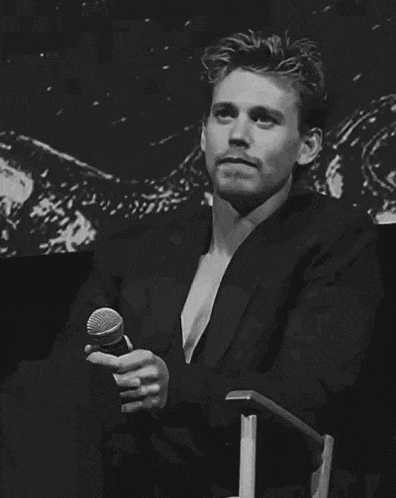 a man in a suit is sitting in a chair holding a microphone and smiling .