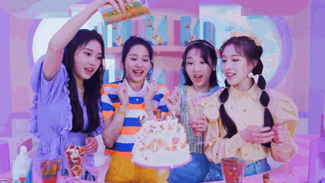 a group of girls are standing around a cake with sprinkles being poured on it