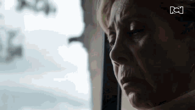 an elderly woman is looking out of a window with her eyes closed .