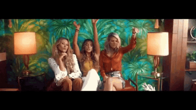 three women are sitting on a couch with their arms in the air in a room .