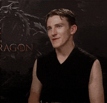a man in a black sleeveless shirt is smiling in front of a dragon poster