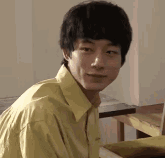 a young man in a yellow shirt is sitting on a couch in a room .