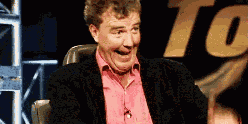 a man in a suit and pink shirt is laughing while sitting in a chair on a stage .