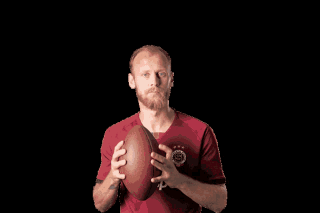 a man in a red shirt that says tip.ort is holding an american football