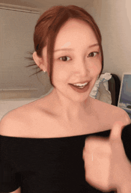 a woman in a black off the shoulder top is smiling and giving a thumbs up