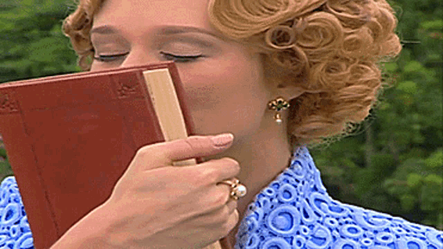 a woman in a blue shirt is holding a book to her face