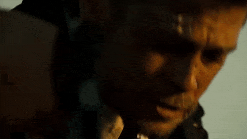 a man with a beard is pointing a gun at the camera in a close up of his face .