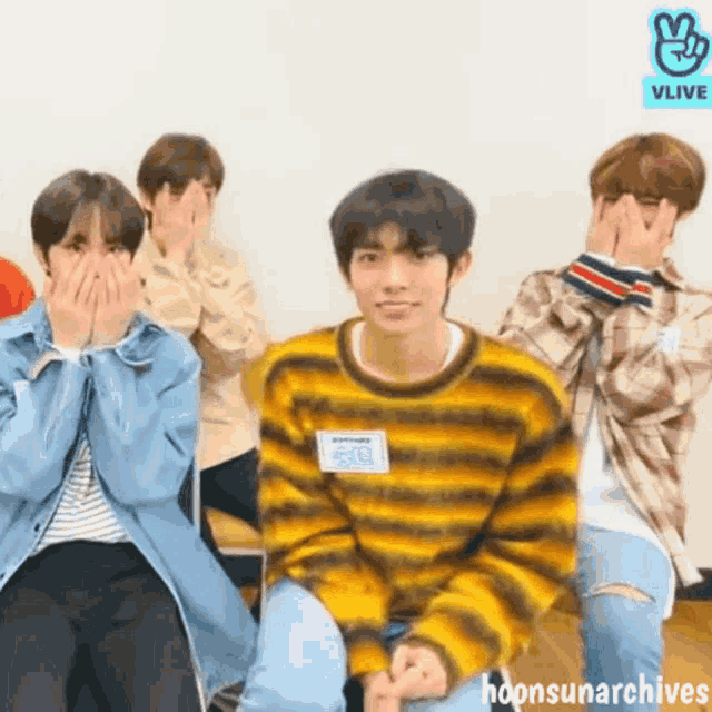 a group of young men are covering their faces with their hands while sitting in a room .
