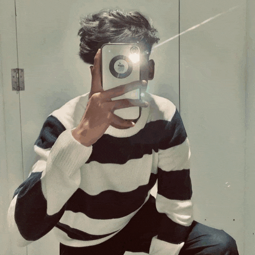 a man in a black and white striped sweater is taking a picture of himself in a mirror