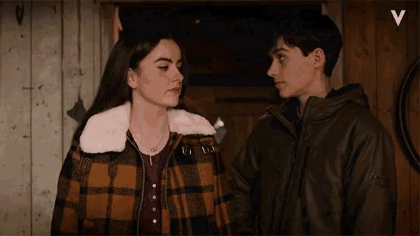 a girl in a plaid jacket stands next to a boy in a green jacket with the letter v above them